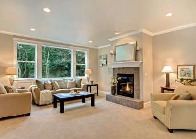 A cozy living room featuring a large sofa, coffee table, and large windows with a view of the outdoor greenery.