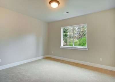 An empty bedroom with neutral-toned walls, soft carpeting, and a large window allowing plenty of natural light.