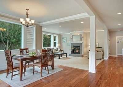 An open dining area with a wooden table set, leading into a living room with a fireplace and hardwood floors.