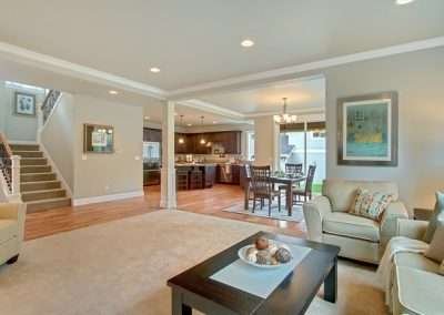 An open-plan living and dining area with beige carpeting, a dining table set, and a kitchen visible in the background.