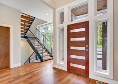 A modern entryway with a wooden staircase and a stylish wooden front door, accented by large windows.