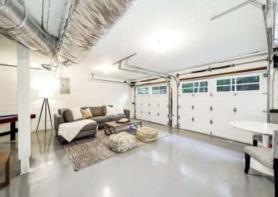 A spacious basement recreation room with a sectional sofa, table, and ample lighting, featuring modern finishes.
