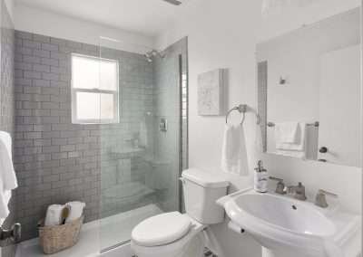 A compact modern bathroom featuring a glass-enclosed shower with grey subway tiles, a white toilet, and patterned tile flooring.