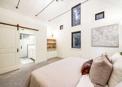 A spacious bedroom with a large bed, windows, and an ensuite bathroom, featuring soft carpeting and modern lighting.