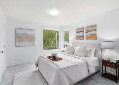 A bright guest room with a bed, bedside table, and large windows