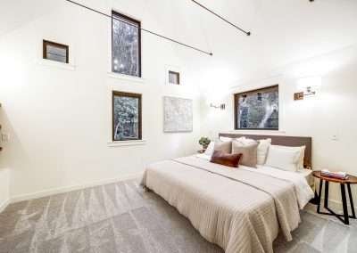 A bright bedroom with multiple windows, a plush bed, and soft carpeting, featuring minimalist decor.