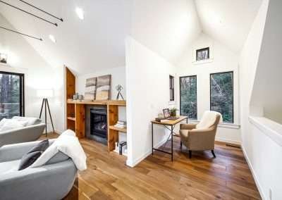A cozy reading nook with a comfortable chair and a small desk, surrounded by large windows with forest views.