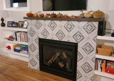 Elegant fireplace decorated for fall, with pumpkins and autumn leaves on the mantel, a TV mounted above, and bookshelves on either side.