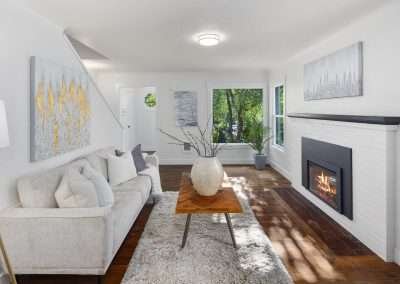 A tastefully decorated living room with a light grey couch, a wooden coffee table, a fireplace, and large windows overlooking greenery
