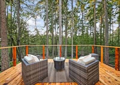 A wooden deck with outdoor seating, surrounded by tall trees and forest views.