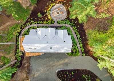 Top view of a modern cabin with a white metal roof and a landscaped garden, surrounded by forest trees.