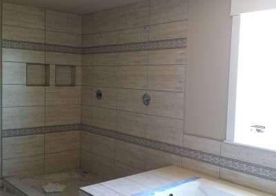 Bathroom renovation in progress featuring a large shower area with beige tiles, decorative brown tile borders, and a bathtub.