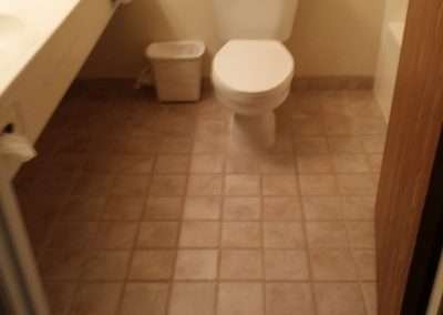 A small bathroom with beige tile flooring, a white toilet, and a white sink vanity.