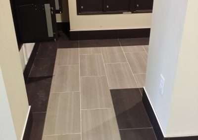 Grey and black tiled hallway in an apartment building with mailboxes and entrance doors.