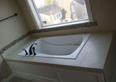 A modern bathtub with a white tile surround and a decorative tile border.