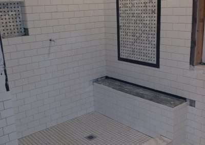 Walk-in shower with white subway tile walls, a marble bench, and a patterned tile accent wall.