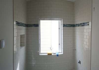 Shower enclosure with white subway tiles and a blue and green mosaic tile border.