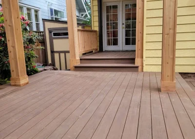 Custom-built composite deck with a wooden pergola and covered entryway, leading to French doors of a Seattle home. Designed by expert deck and patio contractors in Seattle for elegance and durability