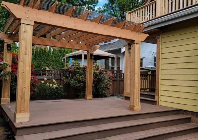 Custom-built wooden pergola with a transparent polycarbonate roof, set on a raised composite deck with wide stairs in a Seattle backyard. Expertly designed by deck and patio contractors in Seattle for enhanced outdoor living