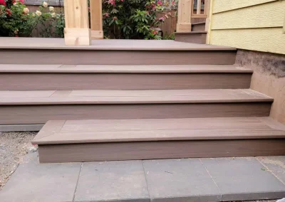 Custom composite deck stairs leading to a covered patio with a wooden pergola, surrounded by lush landscaping in a Seattle backyard. Built by expert deck and patio contractors in Seattle for durability and aesthetic appeal.