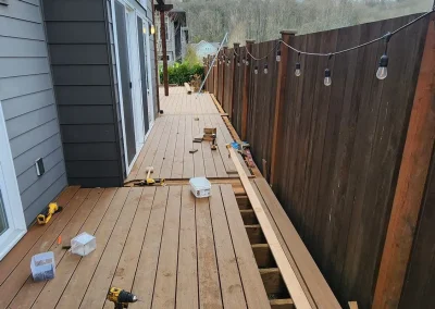 Ongoing composite deck installation along the side of a modern Seattle home, featuring a wooden fence with string lights. Built by expert deck contractors in Seattle for a stylish and functional outdoor space.